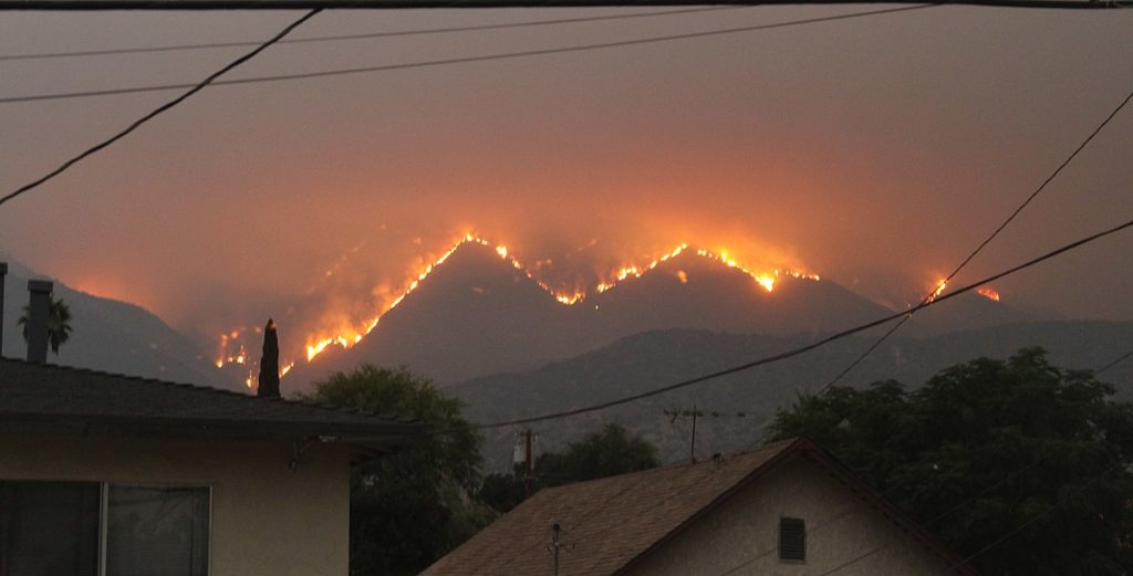 A mountain range with fires all along the top. The lighting is dark/gloomy, maybe it's evening but maybe the smoke is just making everything dark.