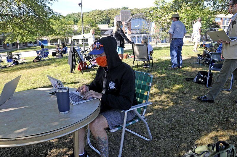 Student wearing mask and hat sits outside on laptop