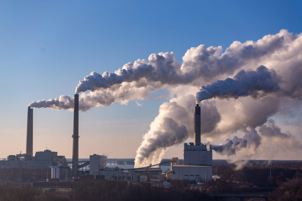 Three smokestacks spewing white-gray vapor into the air against a clear early-morning sky