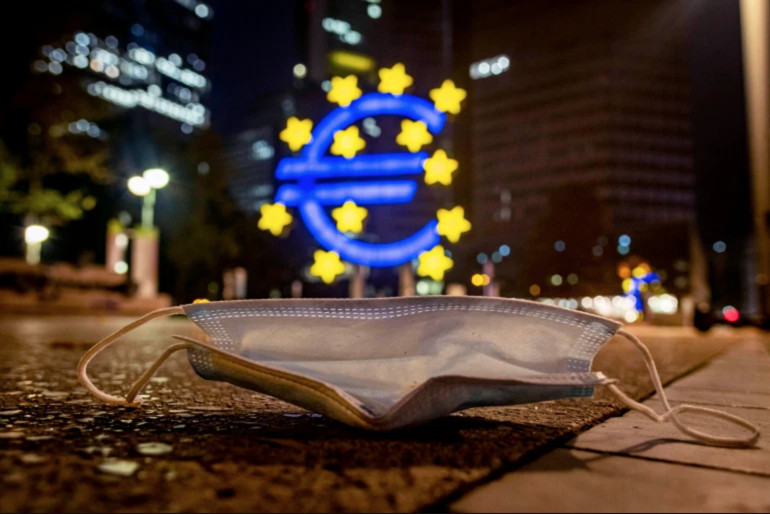 A discarded facemask in front of a large lit Euro sign in Frankfurt