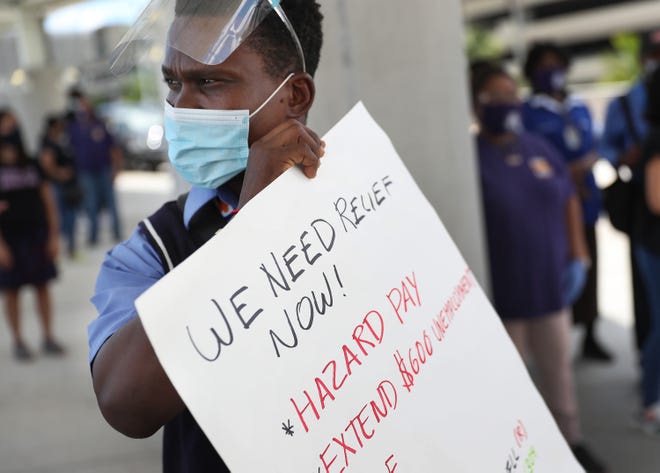 A worker holds a sign demanding hazard pay and extended benefits.