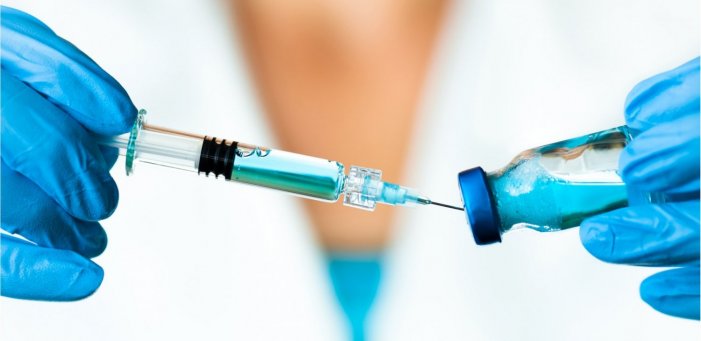 Two hands wearing blue latex gloves hold a vaccine syringe