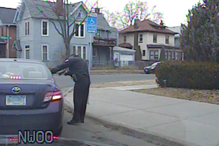 A police officer stands outside a car and points his guns at Somali teens inside in Minneapolis