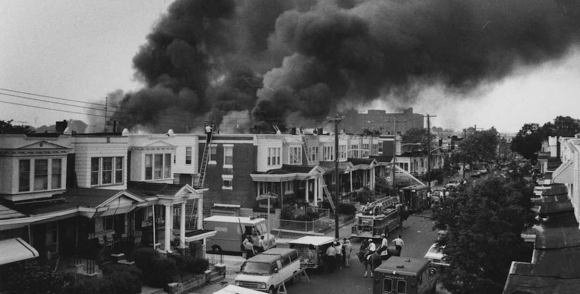 Black and white photo, a street in Philly with smoke in the distance due to the MOVE bombing.