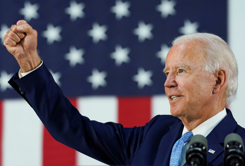 President-Elect Joe Biden stands in front of an American flag, looking to the left, with his right fist raised.
