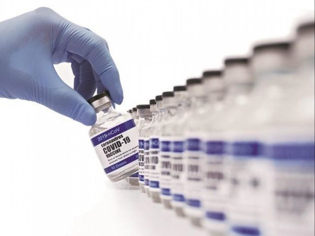 A gloved-hand picks up a Covid-19 vaccine vial from a row of vials