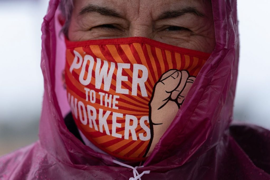 A person wears a face mask with the words Power to the Workers on it along with a clenched fist.