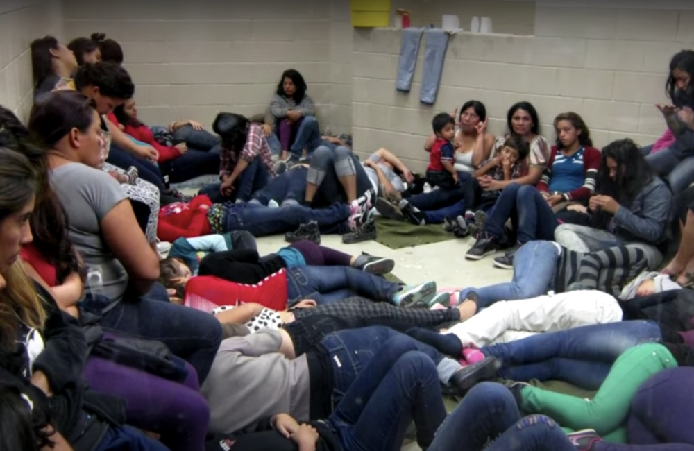The photo shows women and children migrants detained in a large room.