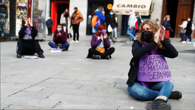 feminist protesters in Madrid sit on the ground holding signs on International Women's Day 2021.