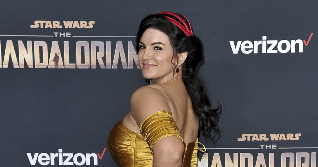 Actor Gina Carano looks back in a yellow dress at an event for The Mandalorian.