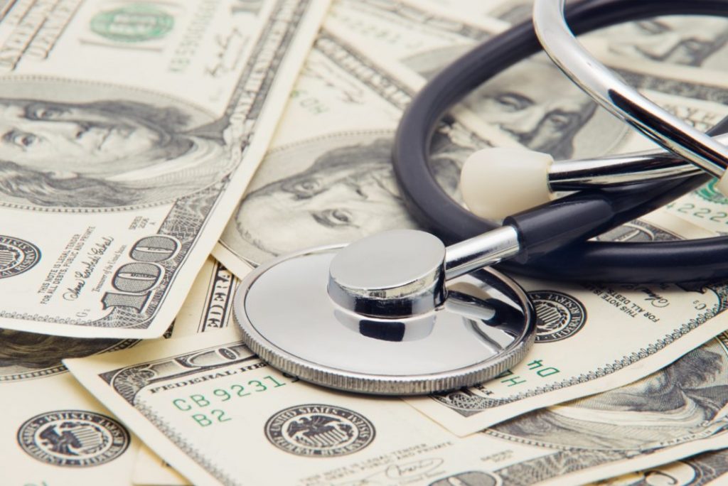 The photo shows a stethoscope atop a bunch of hundred dollar bills.