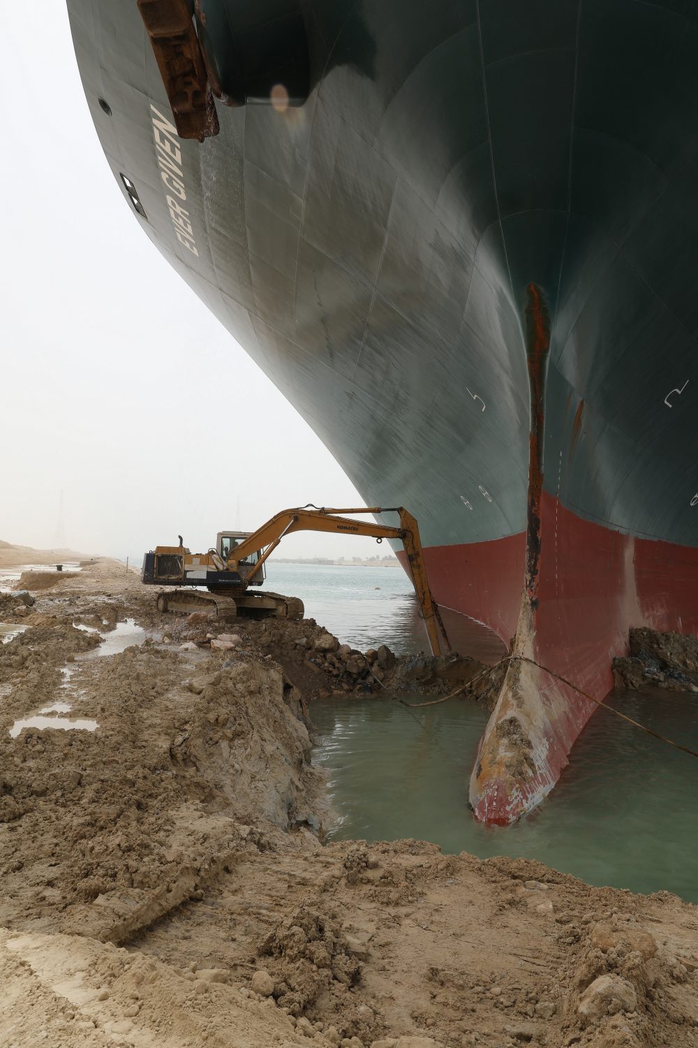 The photo shows a small bulldozer moving earth as it tries to free a huge container ship grounded in the Suez Canal.