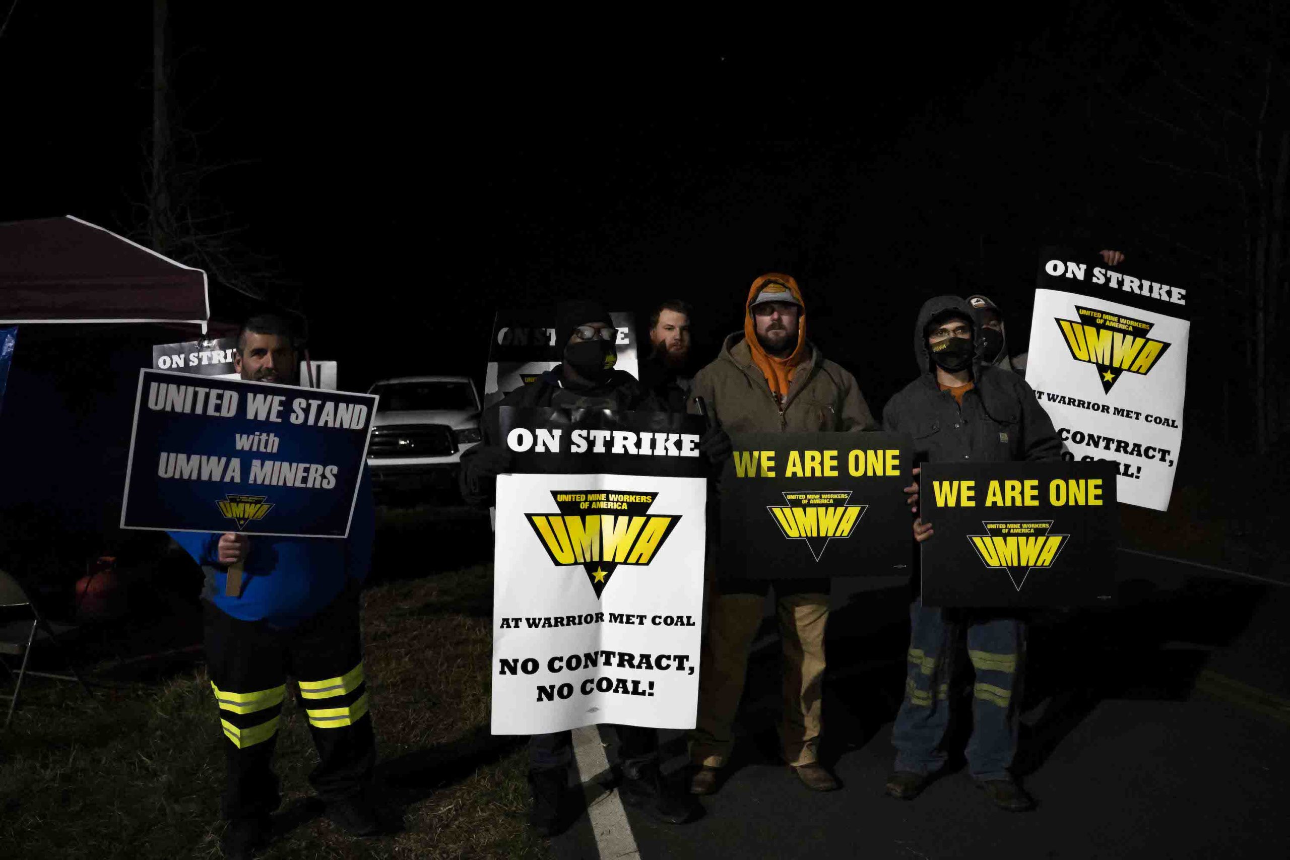 In the dark, striking miners hold up signs saying "No contract, no coal."