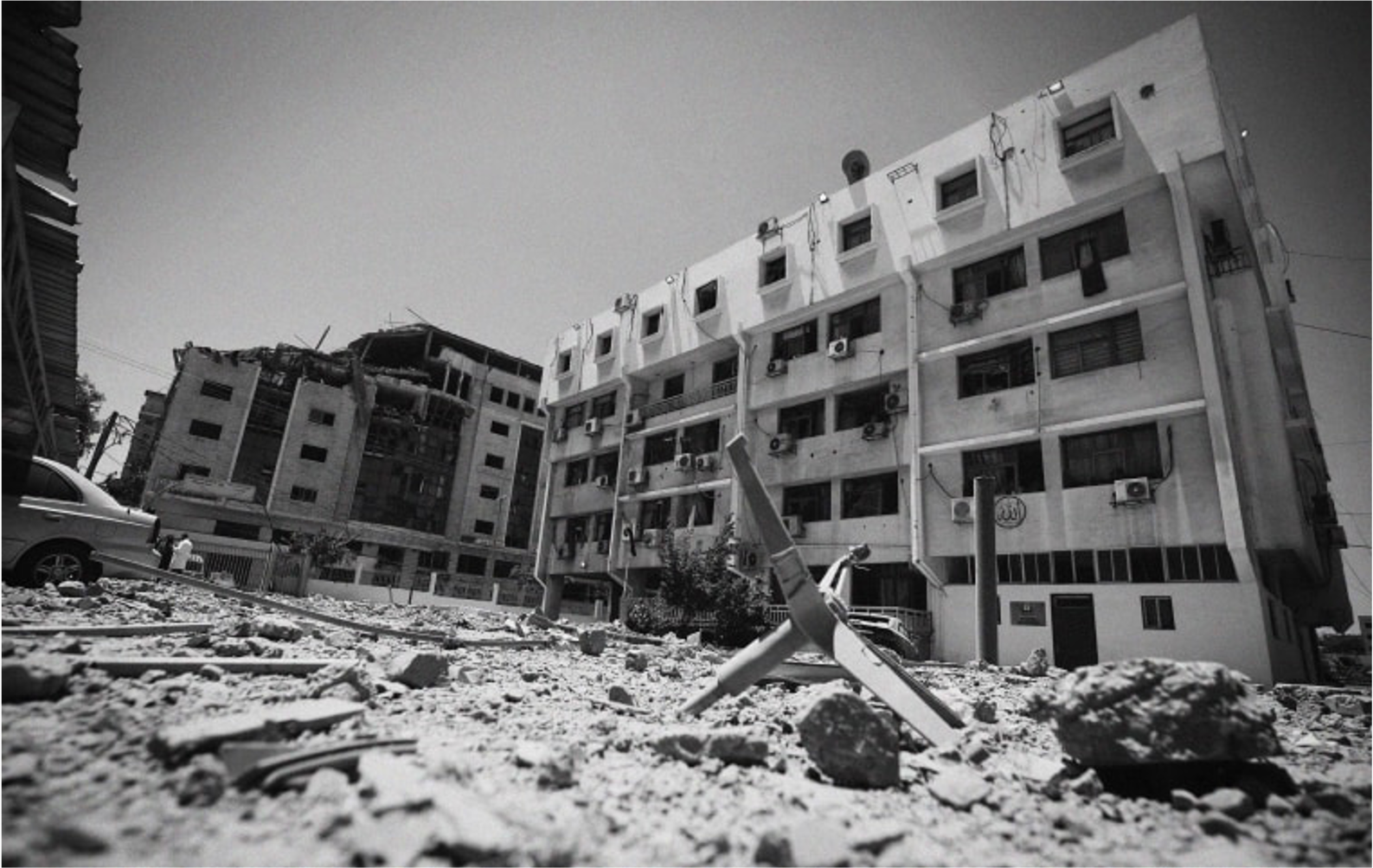 A black and white picture of the Gaza Ministry of Health. The building is damaged, with detritus in front.