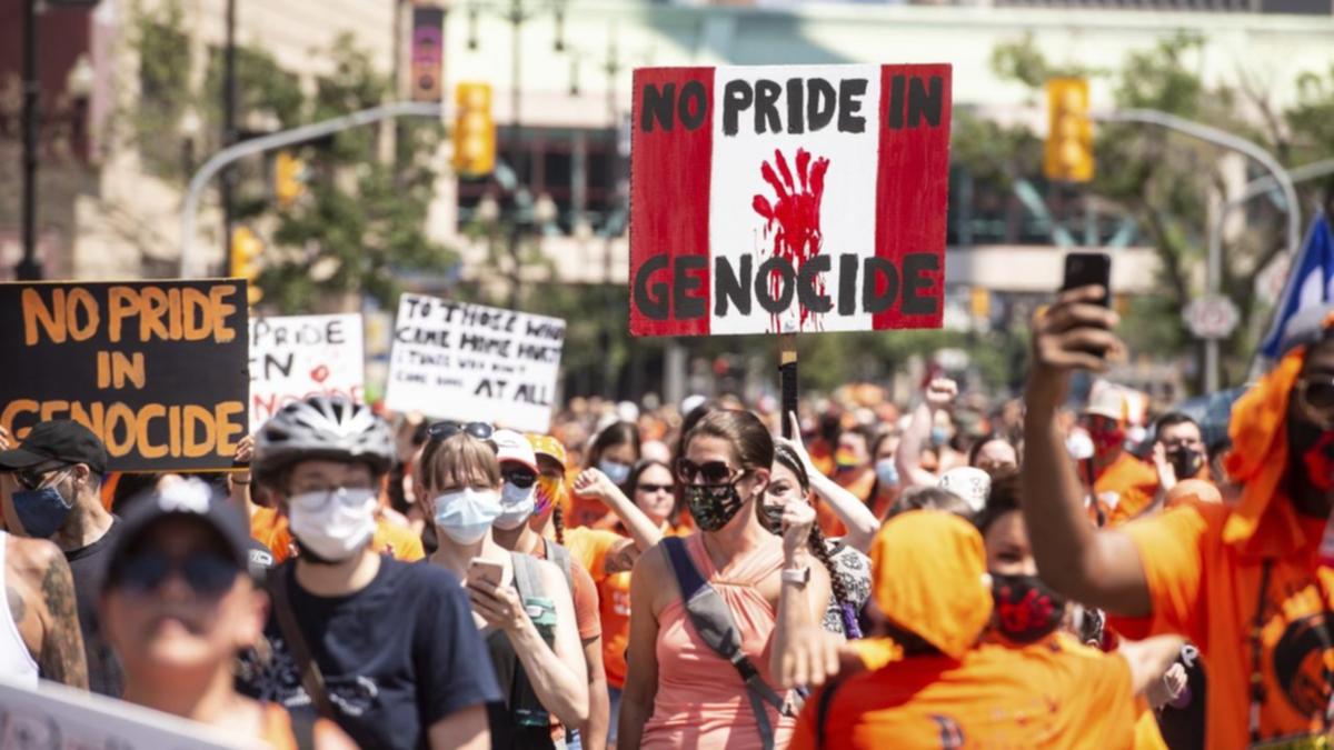 Protesters marching on Canada Day. A sign has the Canadian colors and says "No Pride in Genocide."
