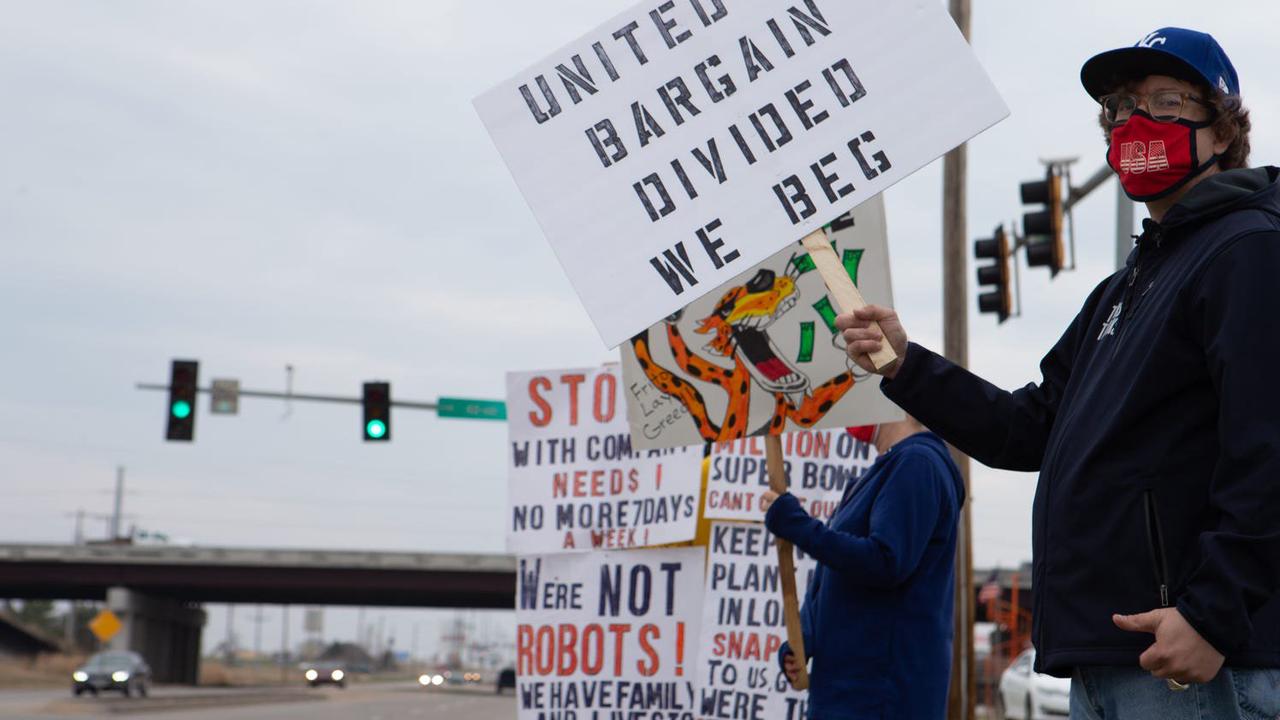 Frito Lay workers stand in front of traffic lights, the one in the front is holding a sign that says "united we bargain, divided we beg."