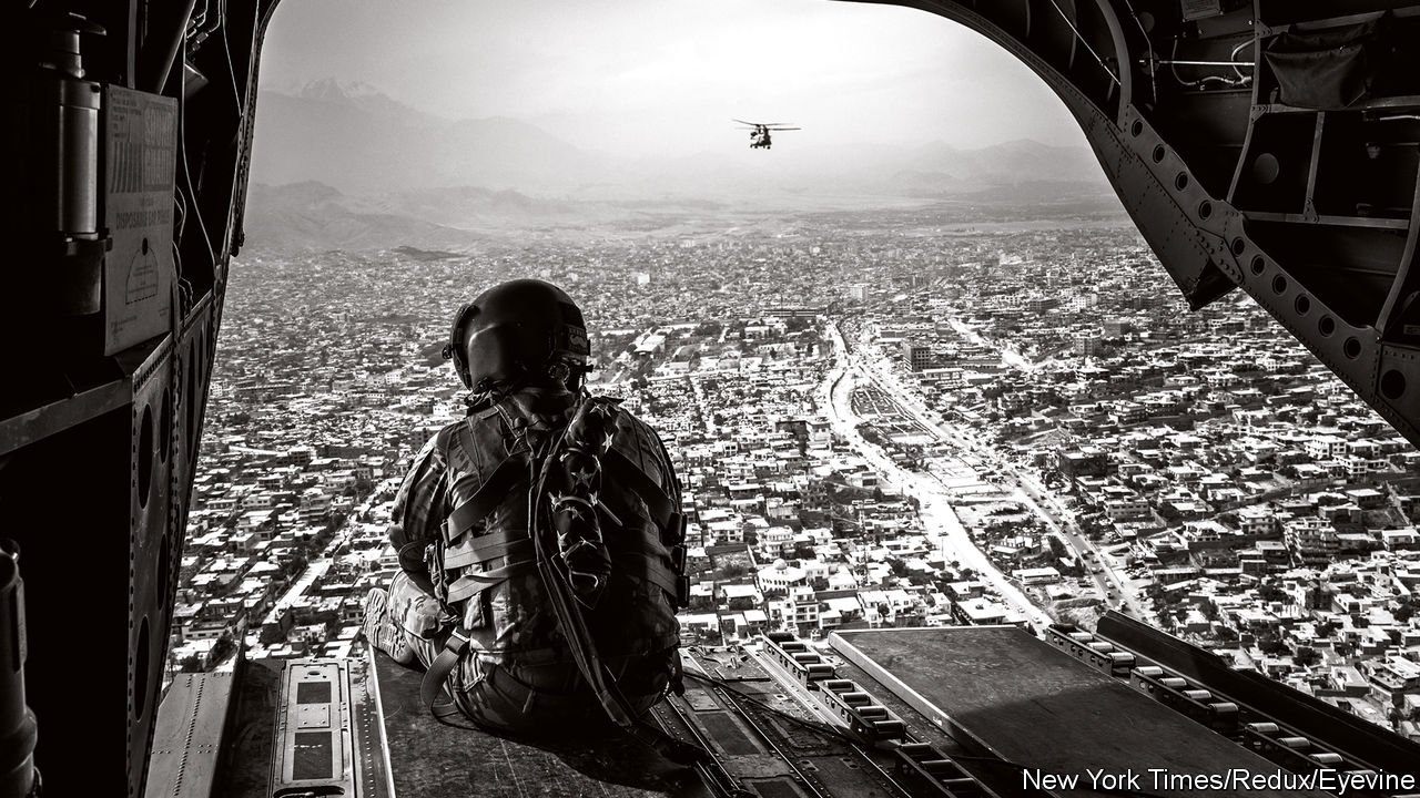 A black and white image of a U.S. soldier looking down at Afghanistan from a helicopter