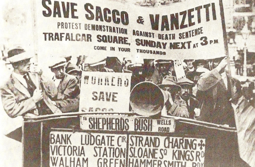 A photo from the 1920s of British workers holding a banner that says "Save Sacco & Vanzetti": Protest Demonstration Against Death Sentence, Trafalgar Square, Sunday Next at 3pm, Come In Your Thousands