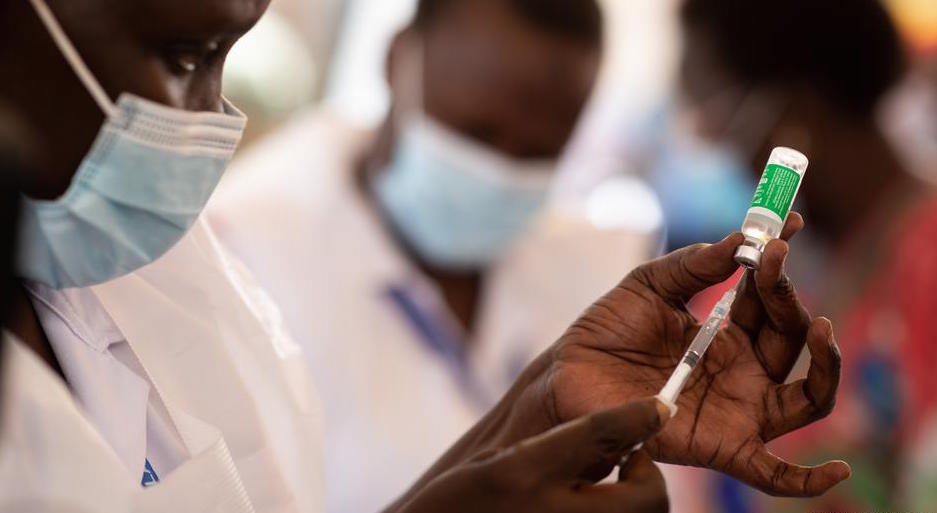 Black person wearing a blue surgical mask injects a syringe into a vaccine vial.