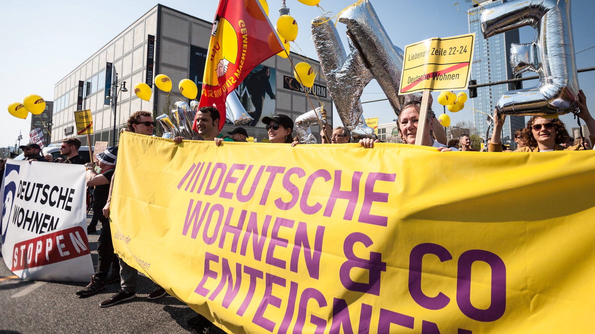 People marching and holding a big yellow and purple banner in favor of expropriating Berlin landlords.