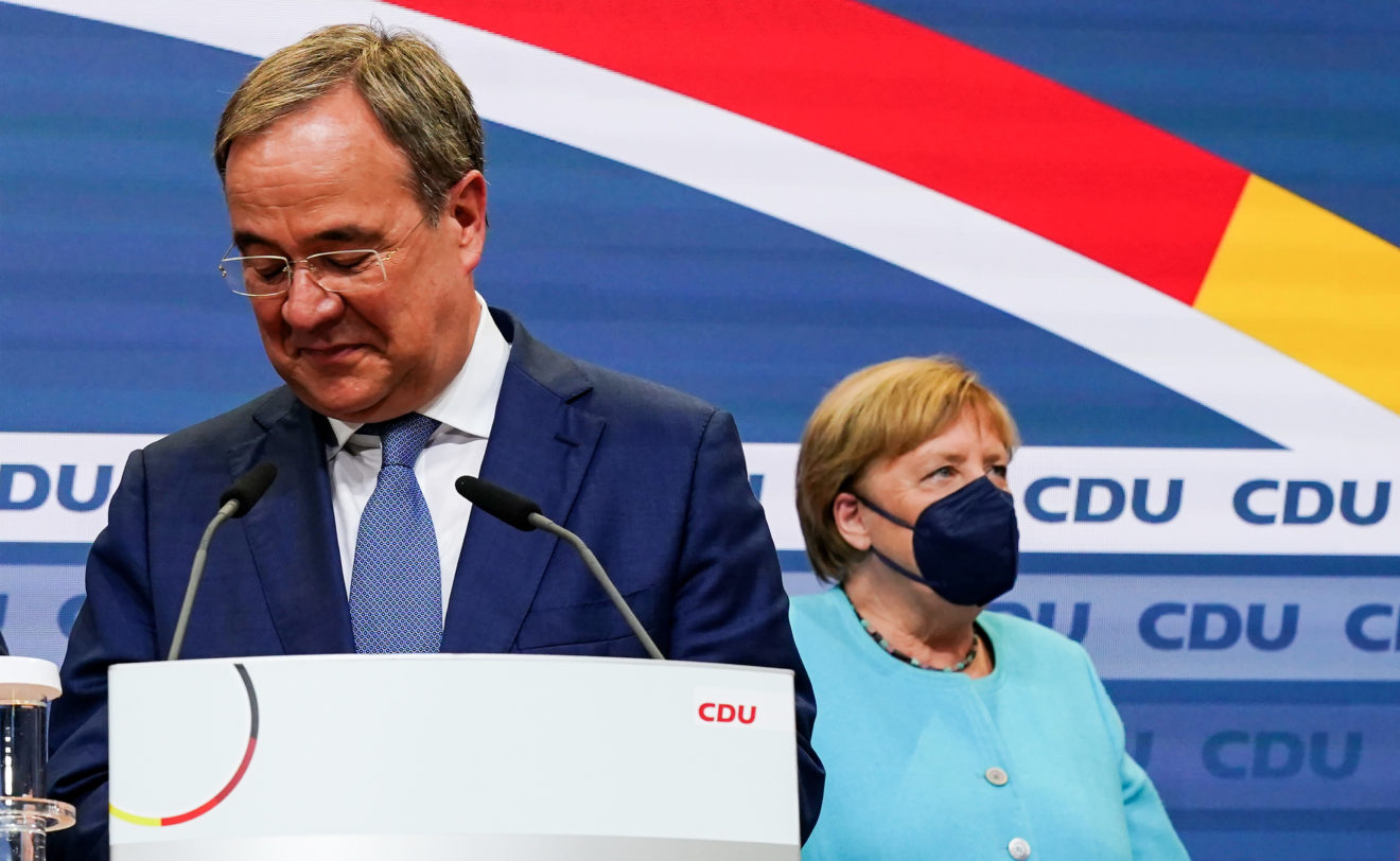 On the left, Armin Lachet, the new leader of the German CDU party. He's a man in his 50s wearing glasses and a suit. In the background, German chancellor Angela Markel wears a mask and light blue suit.