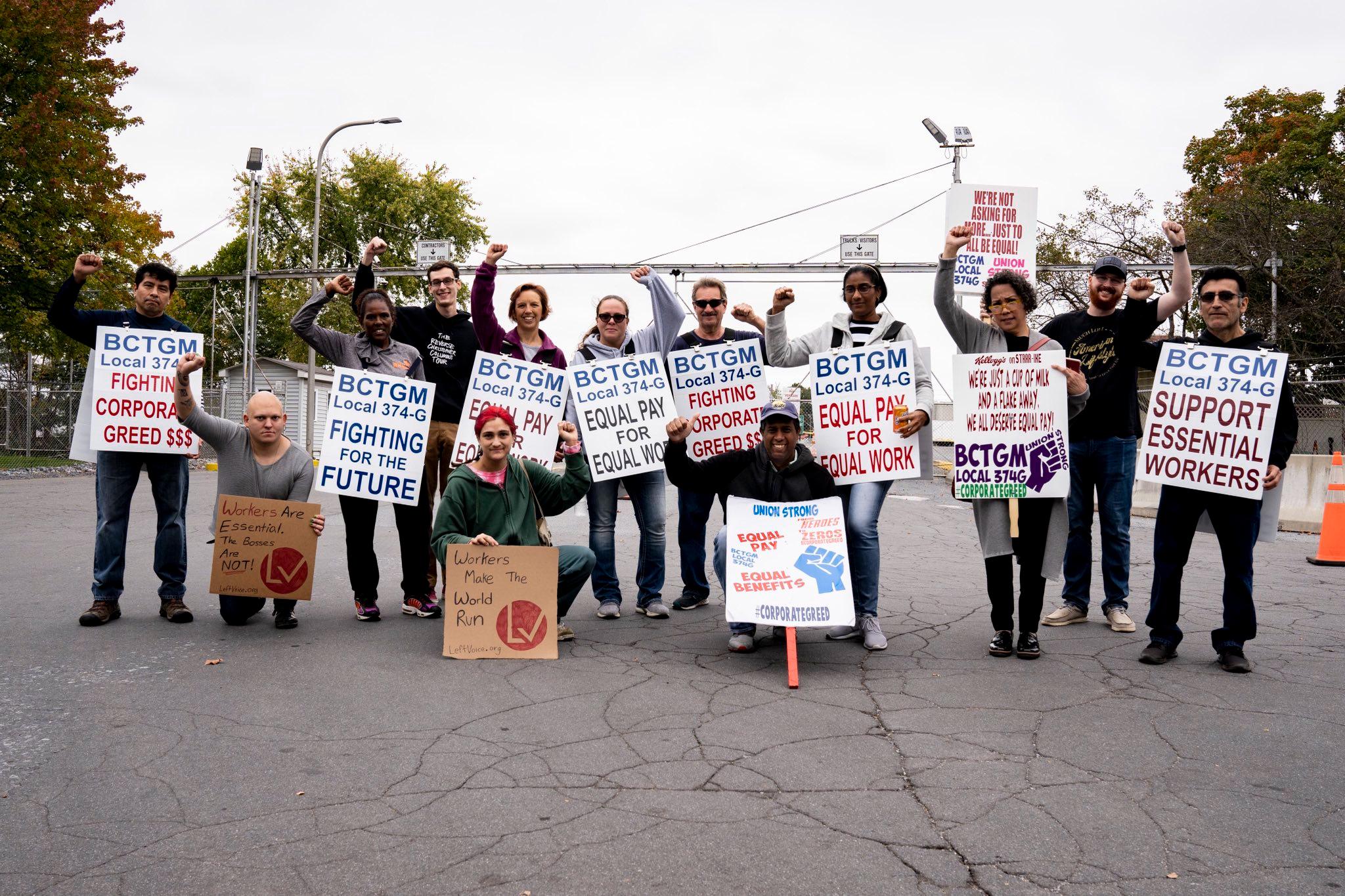 12 people hold signs and hold their fists raised on the Kellogg's picket line.