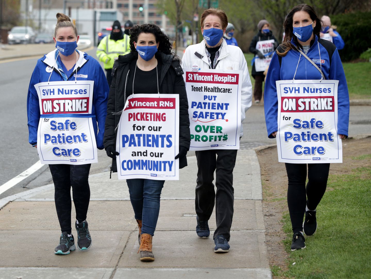 Four female St. Vincent nurses walking side by side on a sidewalk. They are holding signs that read "Safe Patient Care" and "Picketing for our patients and our community."