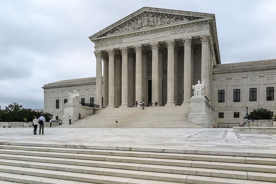 The U.S. Supreme Court building against a cloudy sky. The stairs and plaza in front of the court house are almost entirely empty.