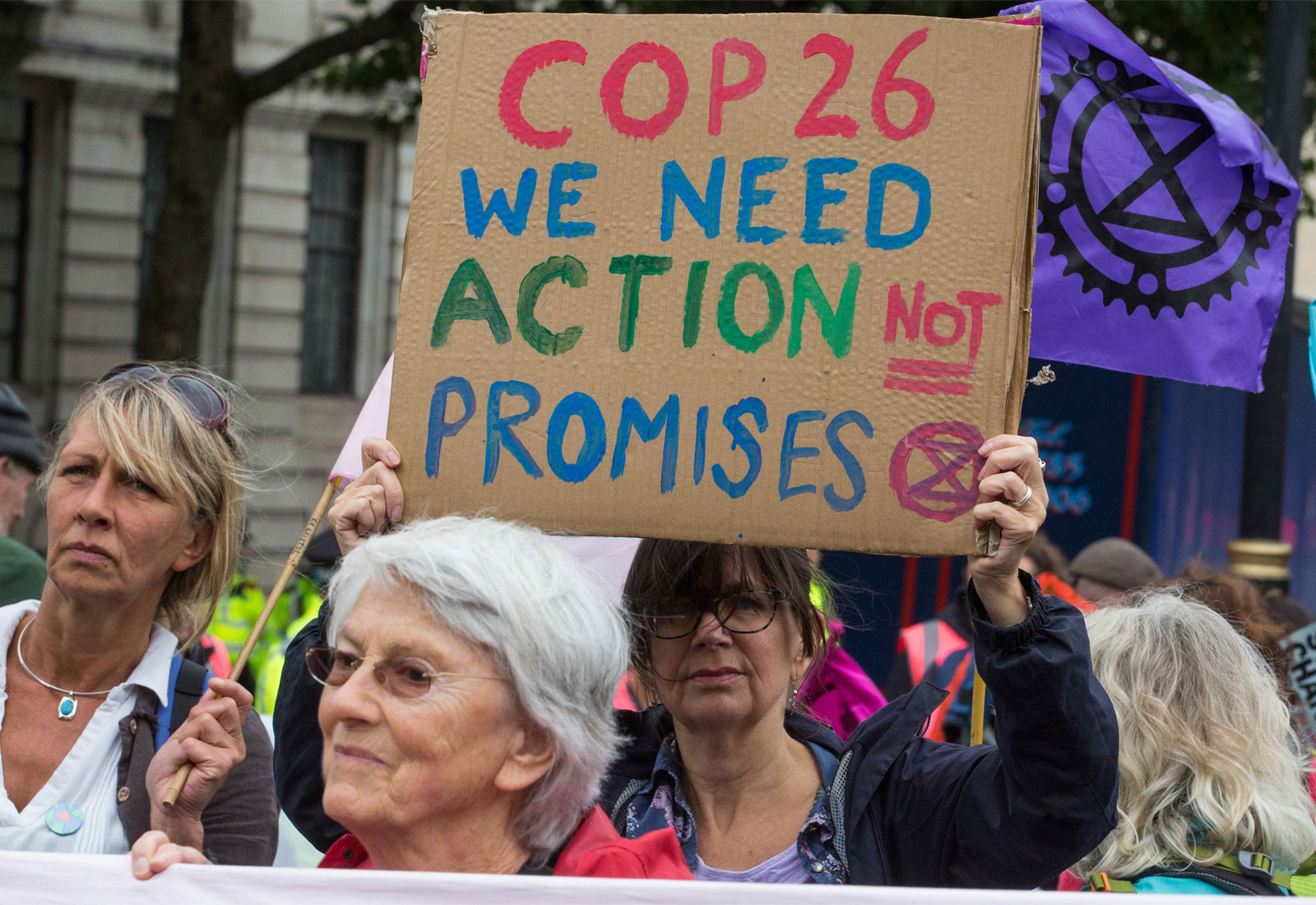 Person with dark brown hair holds up a sign that says "COP 26 WE NEED ACTION NOT PROMISES"