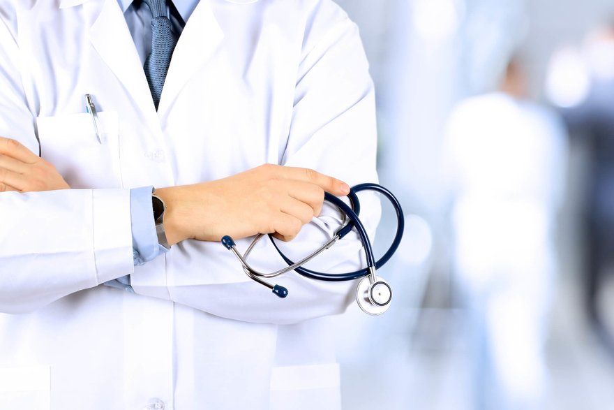Image of person in a white medical coat holding a stethoscope in their left hand and crossing their arms.