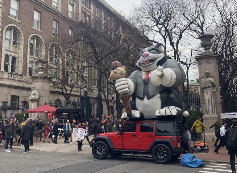 Columbia University on Wednesday December 8. A red car has an inflatable "fat cat" on top which is strangling a worker.