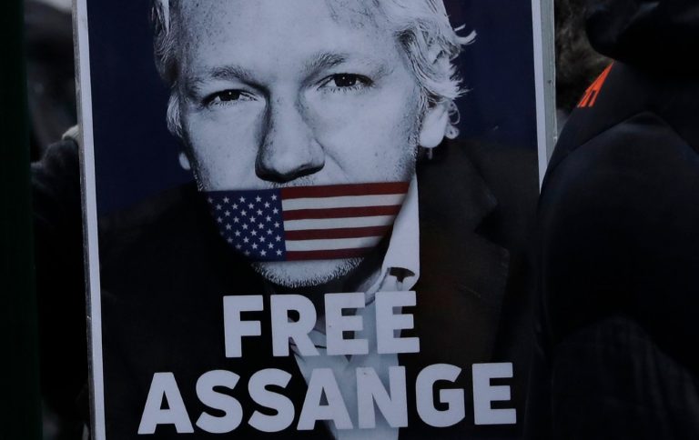 This photo displays Julian Assange with an American flag covering his mouth.
