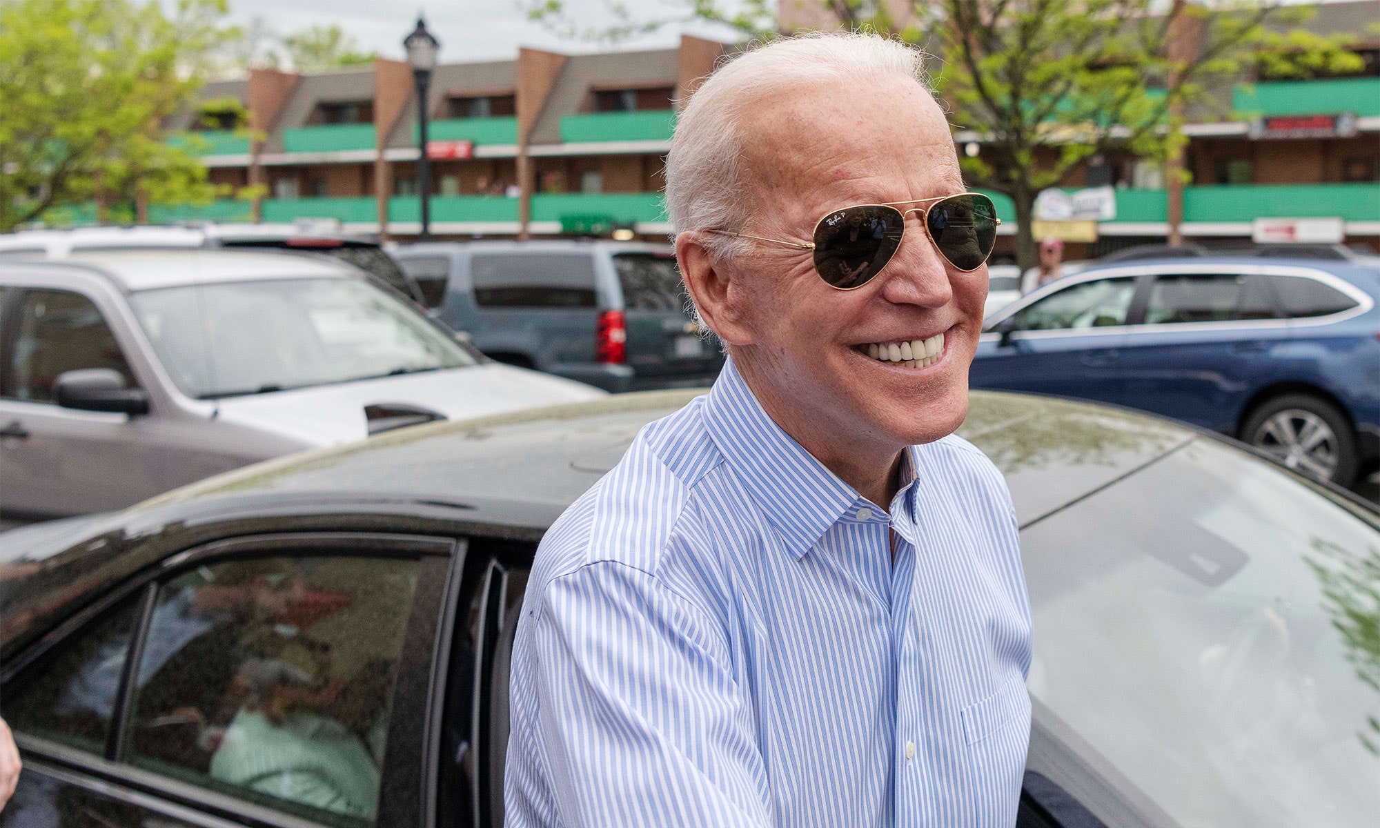 President Biden wears sunglasses, smiling outside.