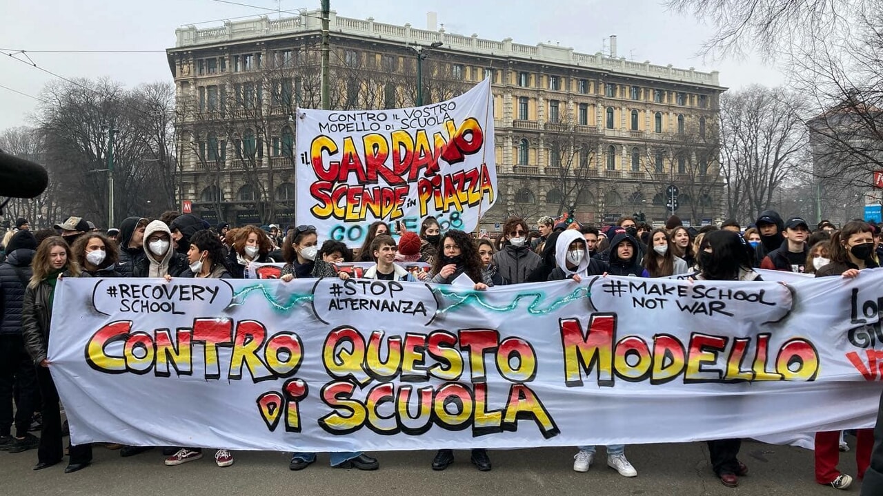 Italian students at a protest stand behind a banner that says “Down with this school model.”