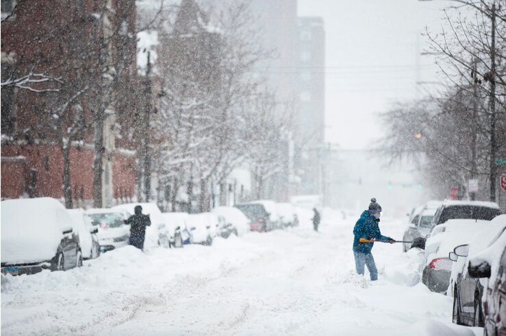 A snowy street in Chicago, people shovel snow.