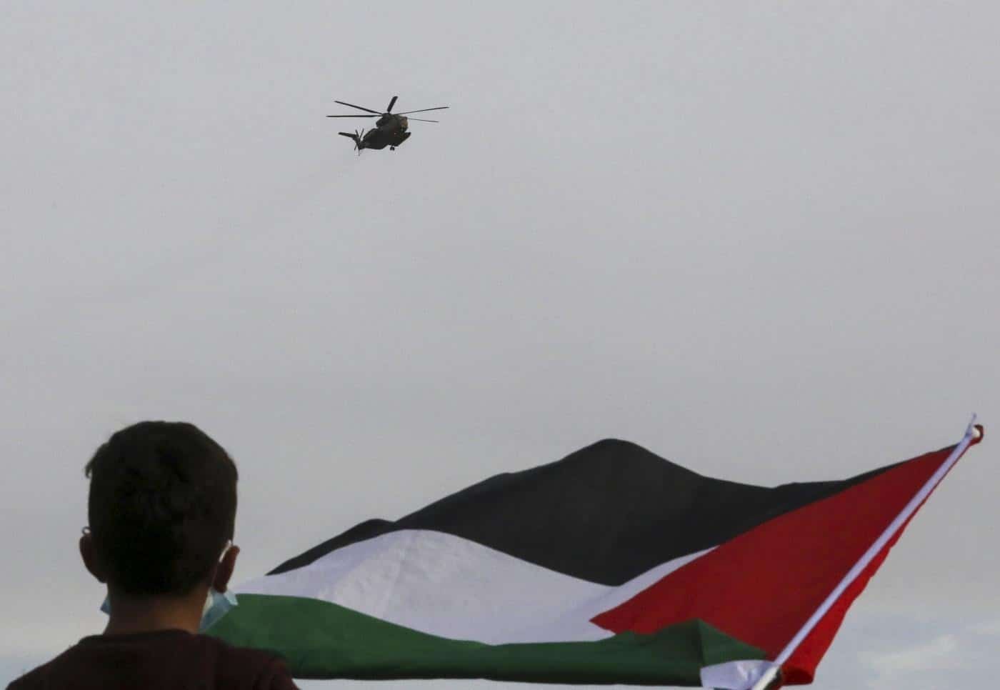 A Palestinian man waves a Palestinian flag as he watches a helicopter over head.