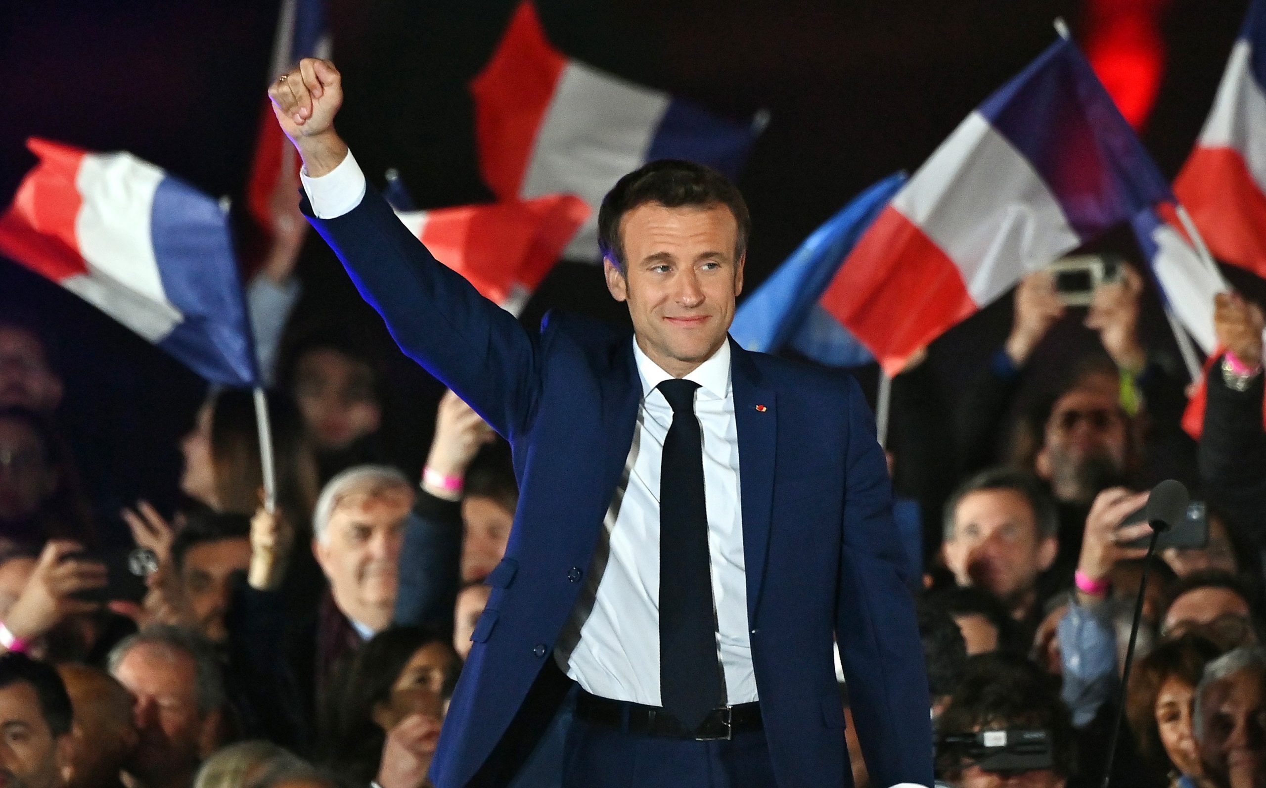 French President Emmanuel Macron raises his fist in front of a crowd of supporters waving French flags.