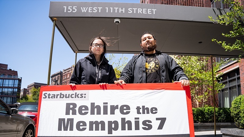 Two Starbucks workers hold sign that reads "Rehire the Memphis 7" u=in front of Shultz' apartment