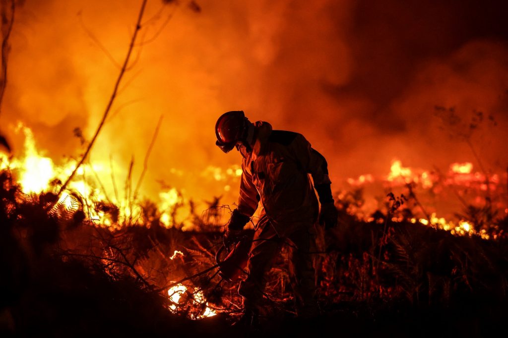 A firefighter in Gironde, France, stands in front of a raging wildfire.
