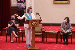 U.S. Speaker of the House Nancy Pelosi speaks at a podium with arms wide open as President of the Republic of China Tsai Ing-Wen looks on.