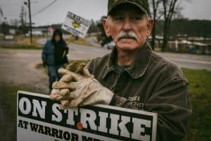 Veteran coal miner holding a sign that reads: on strike