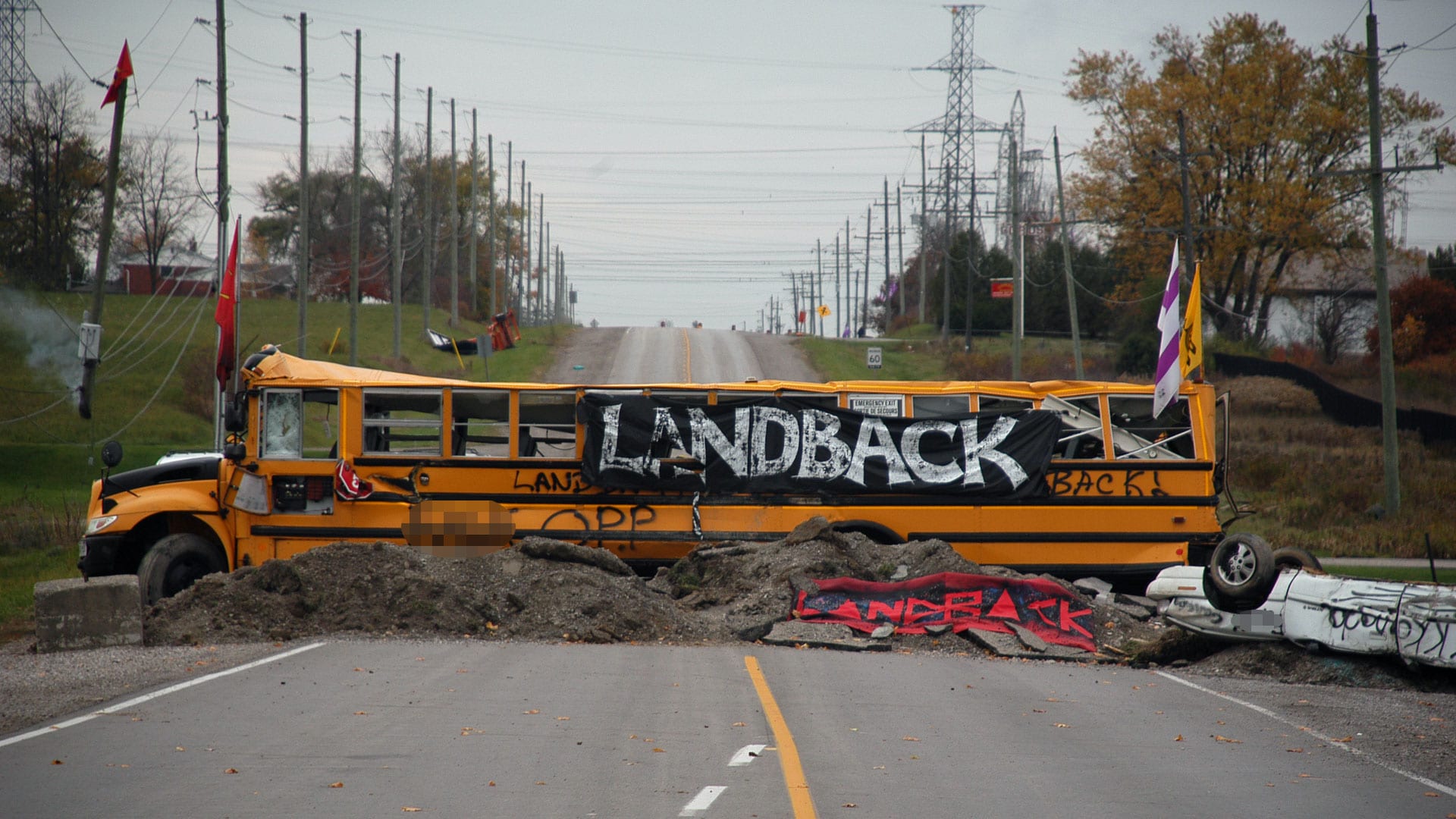 School bus with Land Back banner blocks roadway