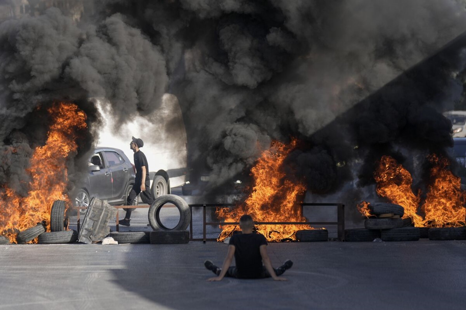 Palestinian protesters sit in front of burning barricades made of tires