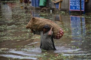 A Pakistani man wades through flood waters carrying a bit bag of produce.