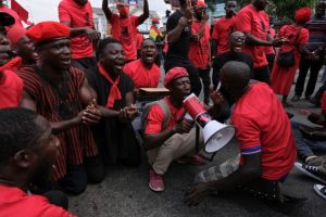 Several Ghanian men dressed in red and black sitting in a circle chanting