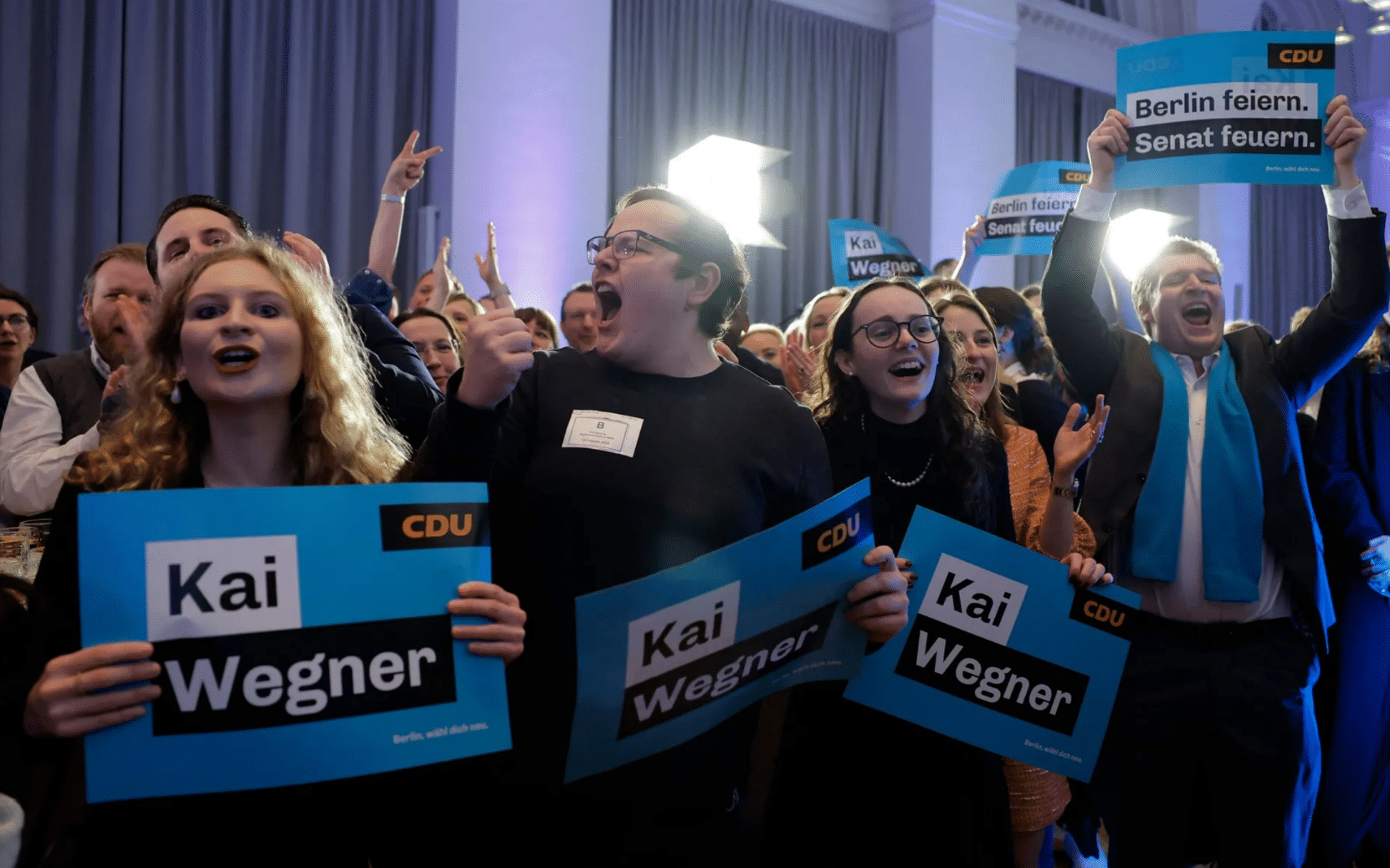 A group of excited people holding campaign signs for Kai Wegner.