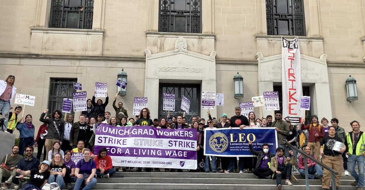 University of Michigan strikers stand outside Rackham Graduate School holding signs.