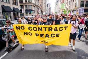 People in New York march on May Day 2022 holding a banner that reads "No contract no peace."
