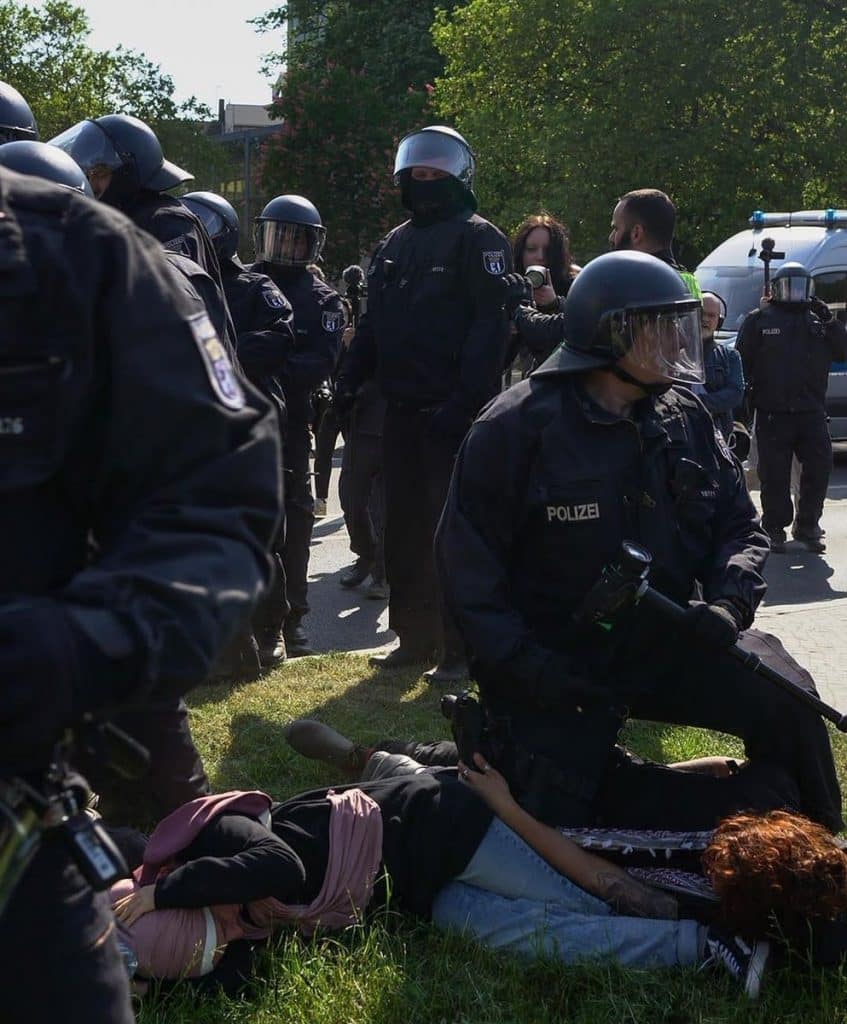 Germany police officers are heavily armed at a Nakhba protest; two protesters are pinned to the ground. 