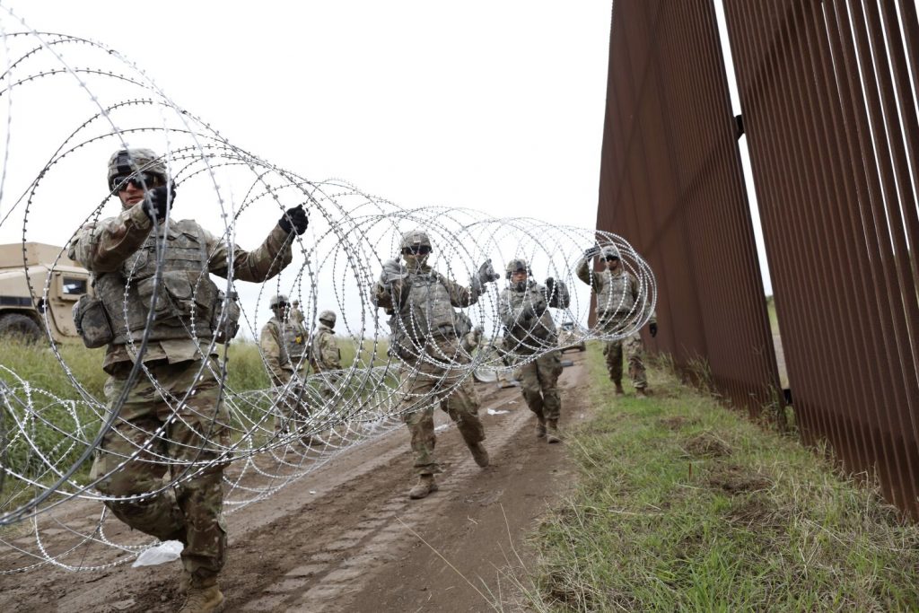 US troops at a southern border wall, setting up barbed wire.